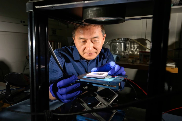 Rochester researcher Ghunlei Guo uses artificial sunlight to test his STEG material, which has been etched with thousands of laser pulses