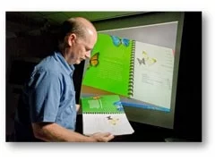 Xerox scientist Rob Rolleston looks over a finished document as Xerox's new 3D Document visualization software displays the document on the screen in the background. (Photo by John Griebsch)