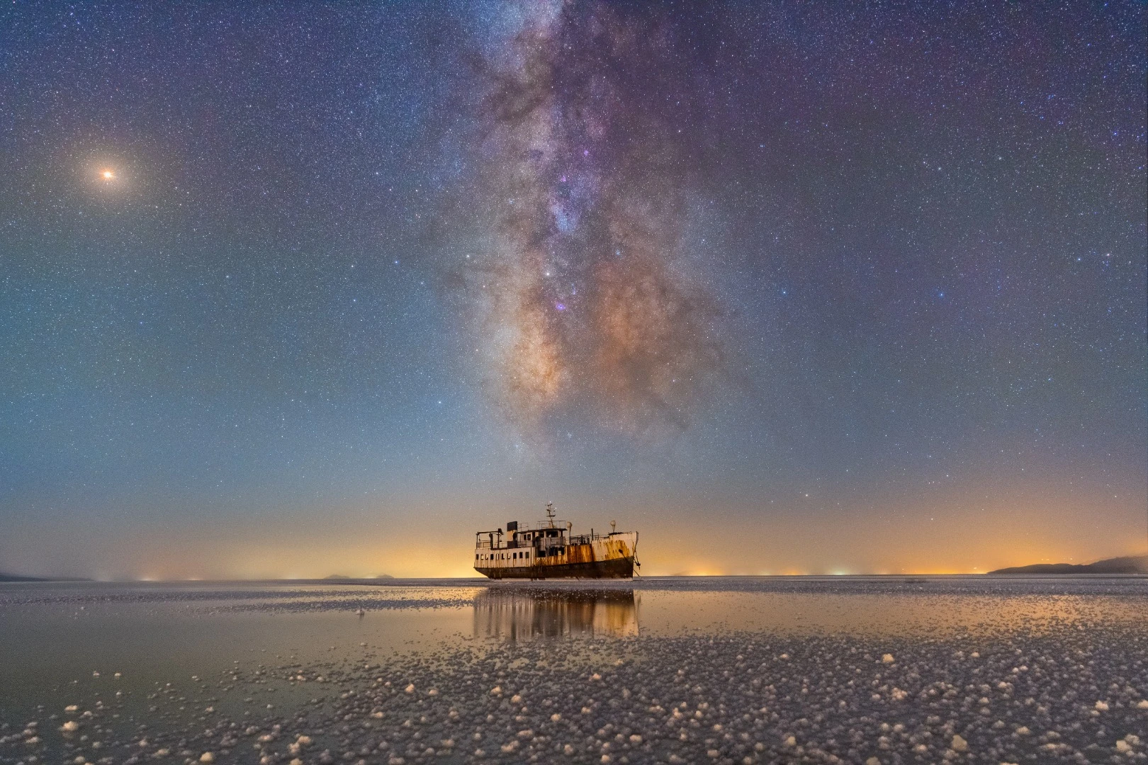 Lake Urmia used to be the largest saltwater lake in the Middle East. Due to climate change, damming of rivers and low rainfall, the lake now contains only five per cent of the amount of water it used to two decades ago. The ship shown was 6 km from the port. Because of the lack of suitable transport, the photographer took a motorcycle for 2.5 km and walked the rest of the way. The summer Milky Way is very prominent in this photo. On the galaxy zone, Saturn is located besides the Lagoon Nebula. On the right of the horizon, you can see the extreme light pollution of Urmia, which is caused by ever-increasing city development.Lake Urmia, Iran, 11 August 2018