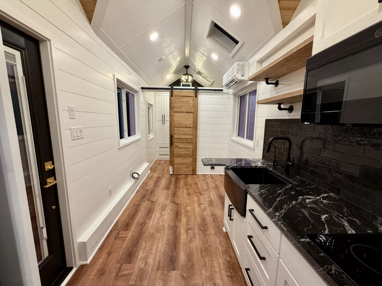The Betty tiny house's kitchen includes a microwave, a two-burner induction cooktop, and a fridge/freezer