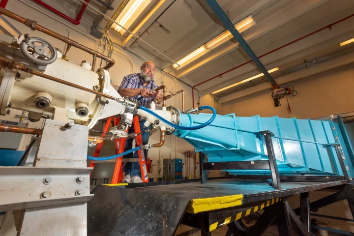 Sandia National Laboratories researcher Leonard Martinez connects a high-voltage-insulating line that circulates oil between a coaxial transmission line (white tube on the left) and the blue oil-filled transmission horn. of the EMES machine