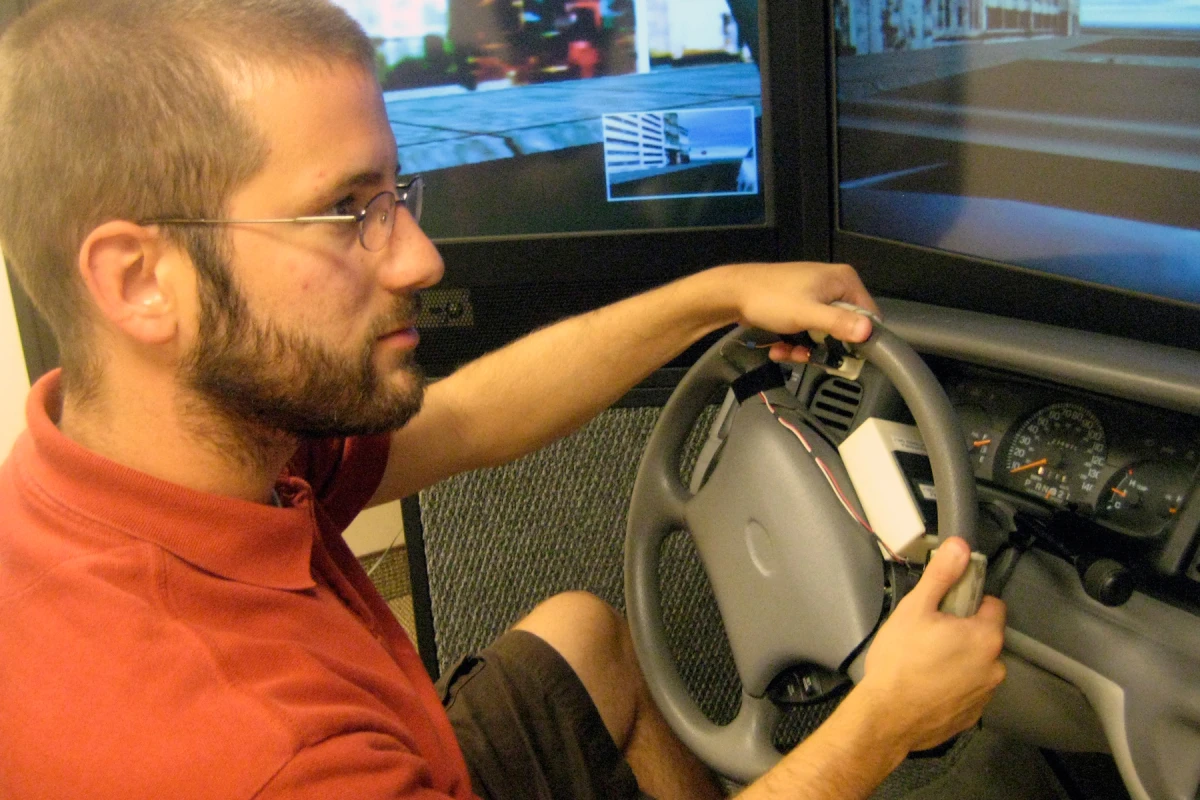 University of Utah psychology doctoral student, Nate Medeiros-Ward, operates a driving simulator with a steering wheel equipped with two touch devices that pull the skin on his index fingertips left or right (Image: Justin Lukas, University of Utah)