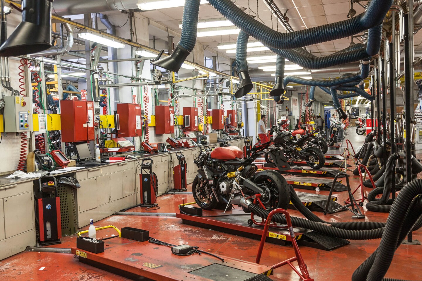 Emissions testing area. Collection pipes gather exhaust gases for analysis, and the vacuum pipes above the bikes remove petrol fumes from the working area.