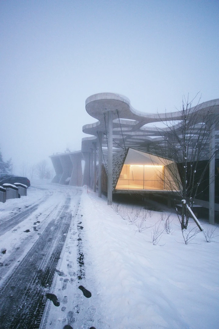 The "Suspended Forest" cabin hangs from a large overhead concrete structure, allowing the dwelling to hover above the snow-covered landscape