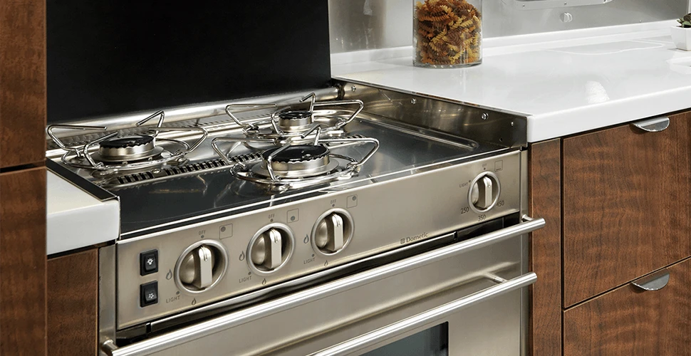 A stainless steel sink is sunk into Corian countertops alongside a three-burner stove, 6.7 cubic ft fridge and slide-out pantry