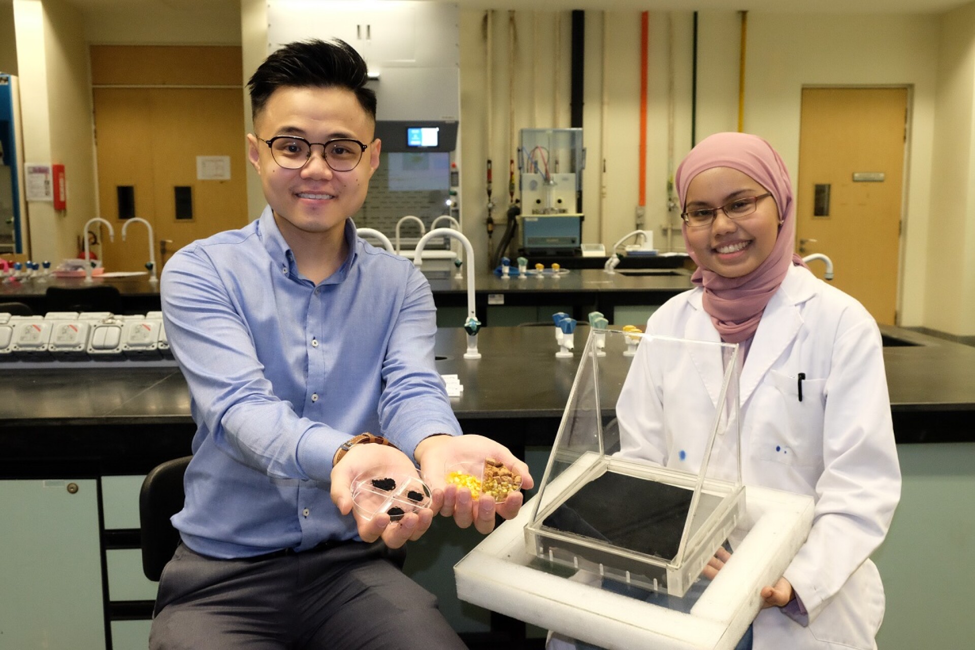From Fruit Waste To Water-purifying Material Assistant Professor Edison Ang from Nanyang Technological University, seen on the left, displays samples of both fruit waste and molybdenum carbide. One of his colleagues demonstrates a solar still containing a black sheet made of the aforementioned material.