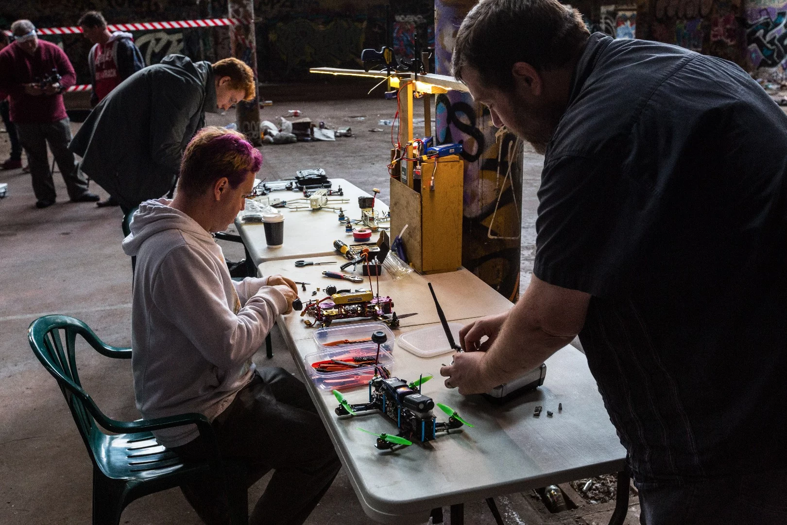 Onlookers lounge in camping chairs and nurse cups of hot tea while off-duty racers wrangle soldering irons and tinker with their machines in the background