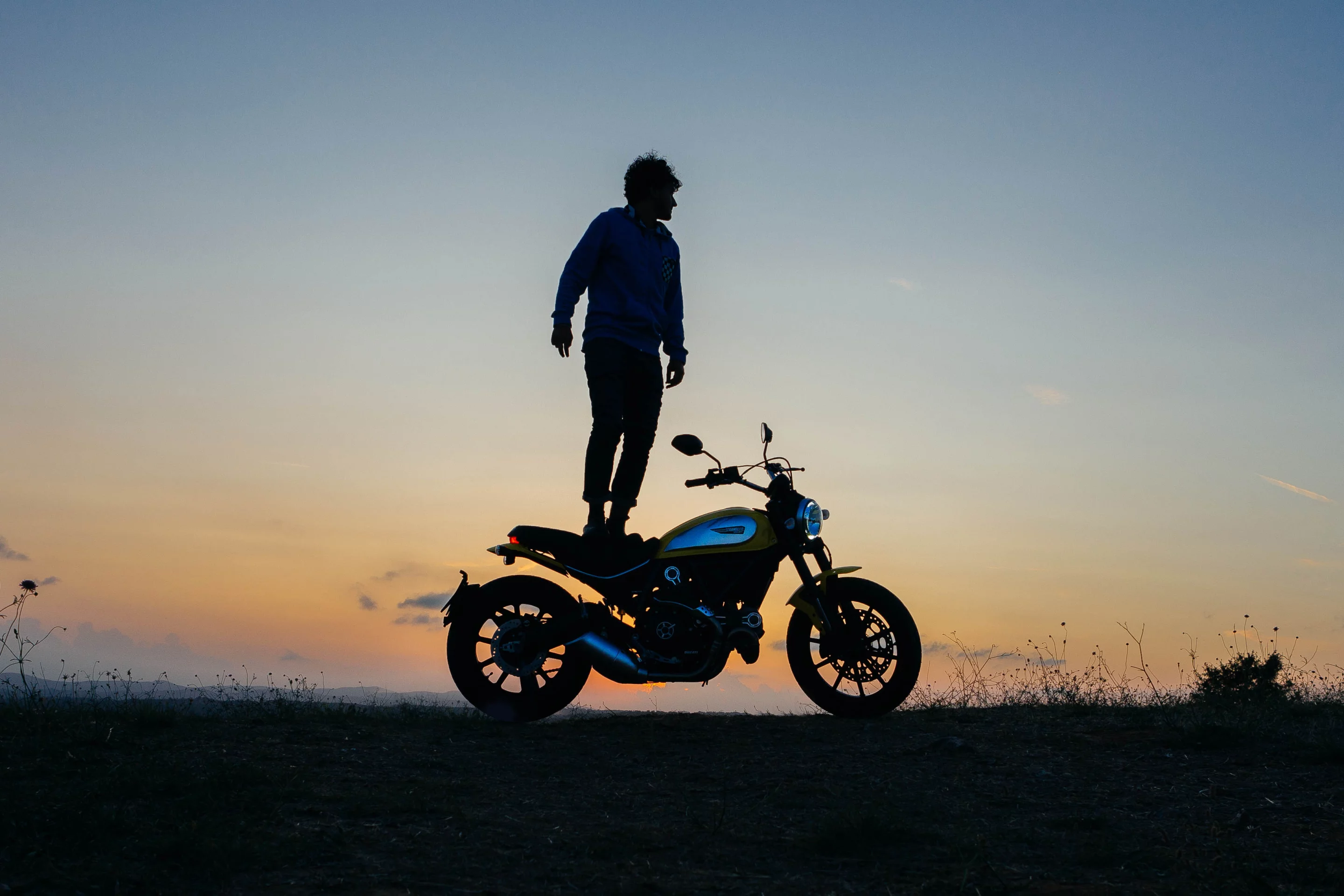 Man stands on Ducati Scrambler at sunset