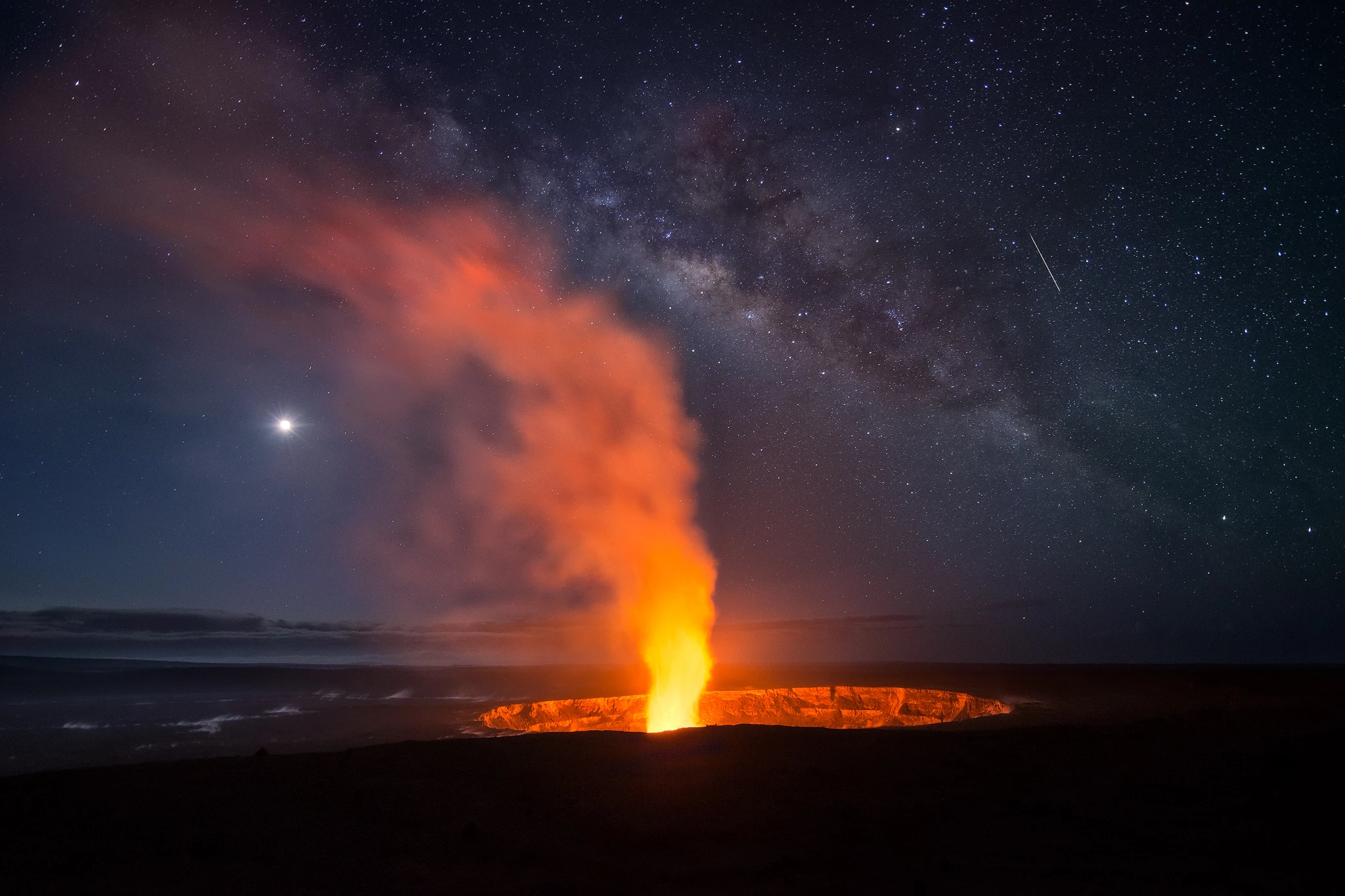 Elemental, shot in Hawaii, USA. The Milky Way lines up with the plume at the Halema'uma'u crater in Kilauea Volcano. The Moon glows off to the left, and a meteor streaks by on the right.