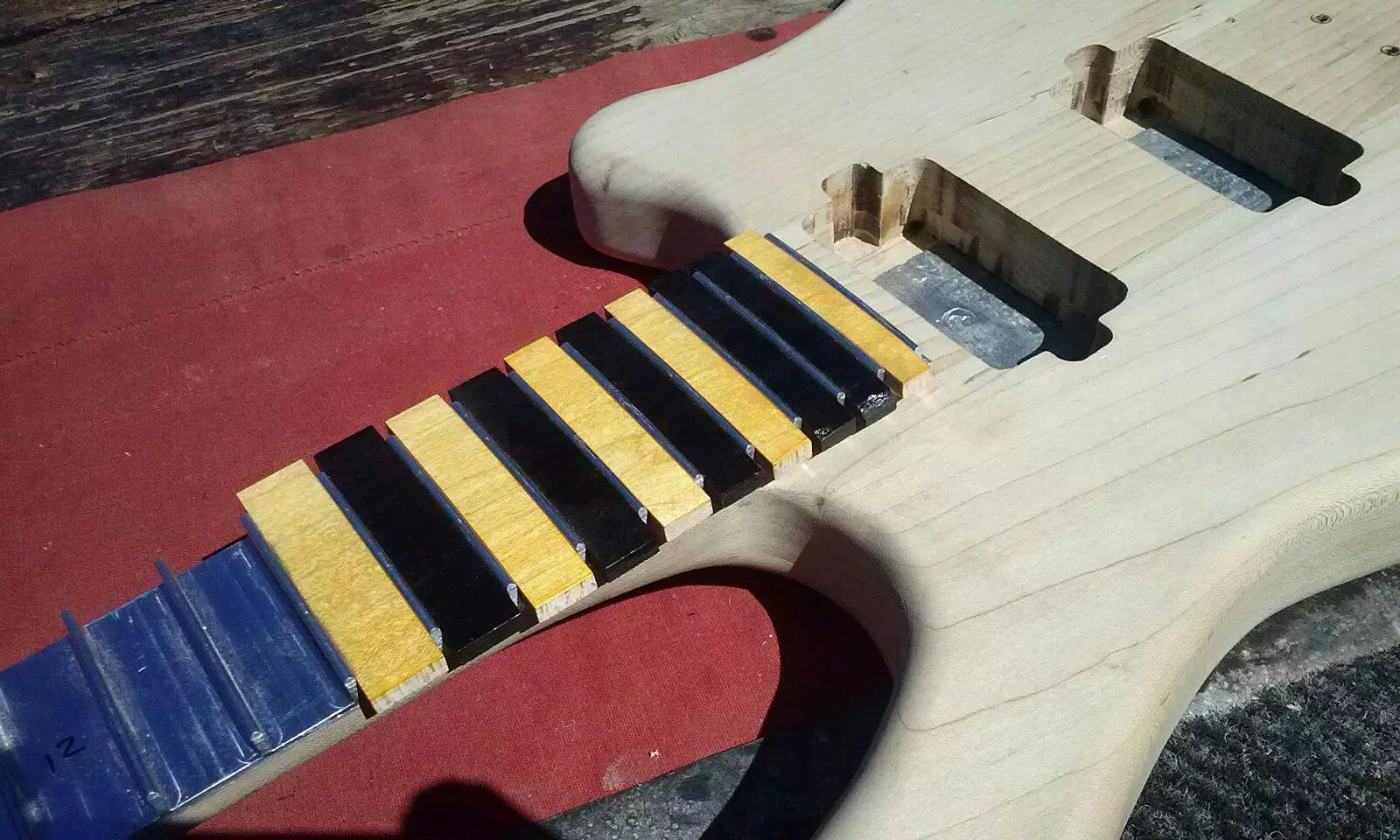 A single block of aluminum alloy is machined to create precisely positioned frets standing up from a metal back plate, with bits of wood slotted in and finished to form the fingerboard