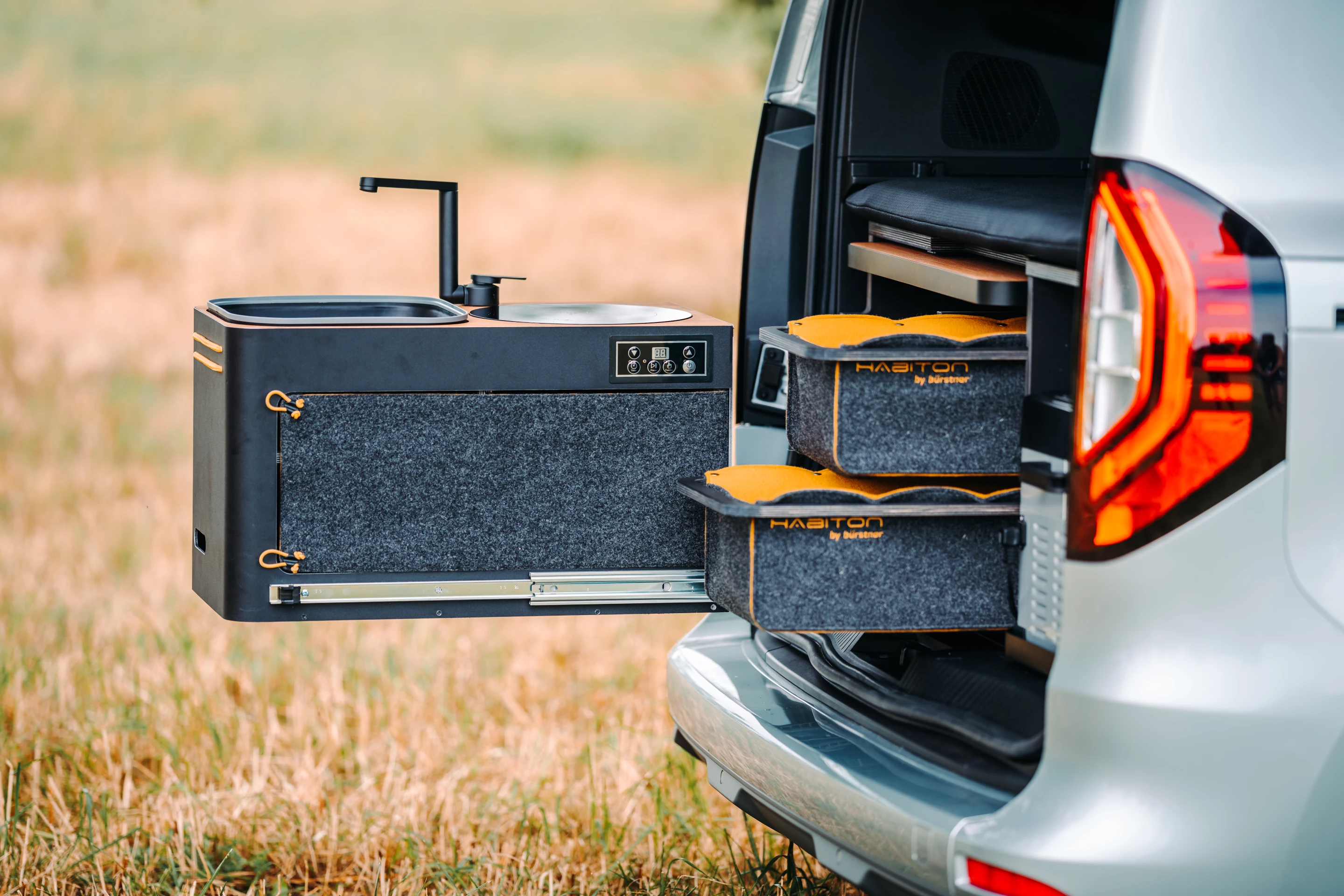 The slide-out kitchen includes an induction cooktop, sink, fridge and storage drawers