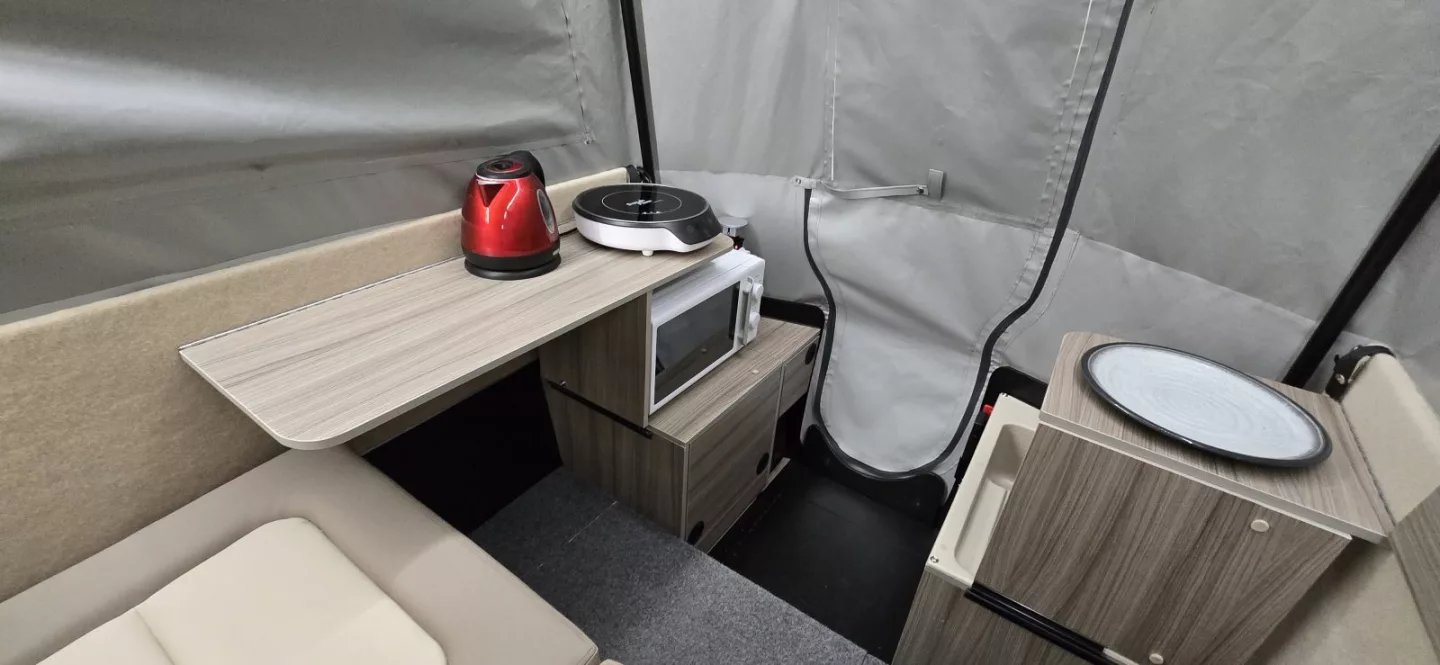The left and right fold down shelves also serve as individual dining tables and desktops for the two campers seated in the Dashaway ECT 2 camping trailer