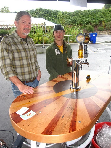 The Beer Bike is a custom-built cargo bicycle that features two beer kegs, a wooden bar with two serving taps, space for pizza boxes, and a solar-powered boom box