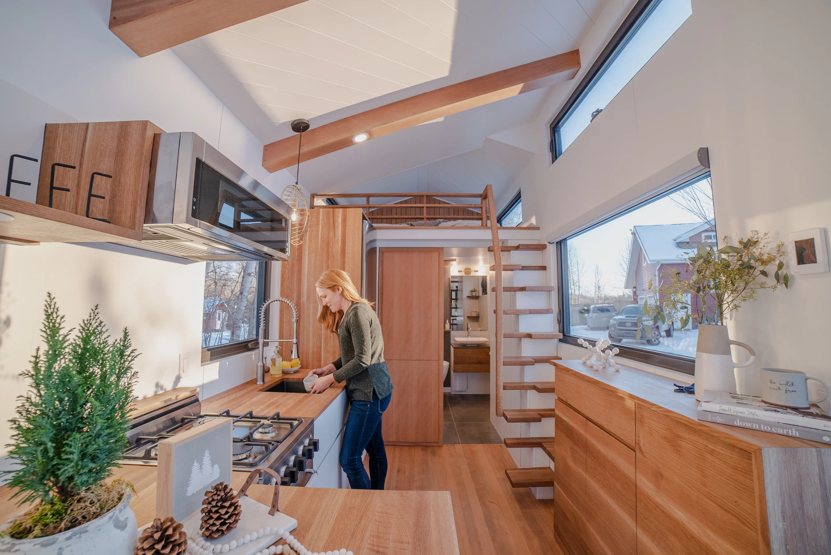 The tiny house features a central full-sized modern kitchen with stainless steel appliances, a bar-style seating bench and hidden European laundry