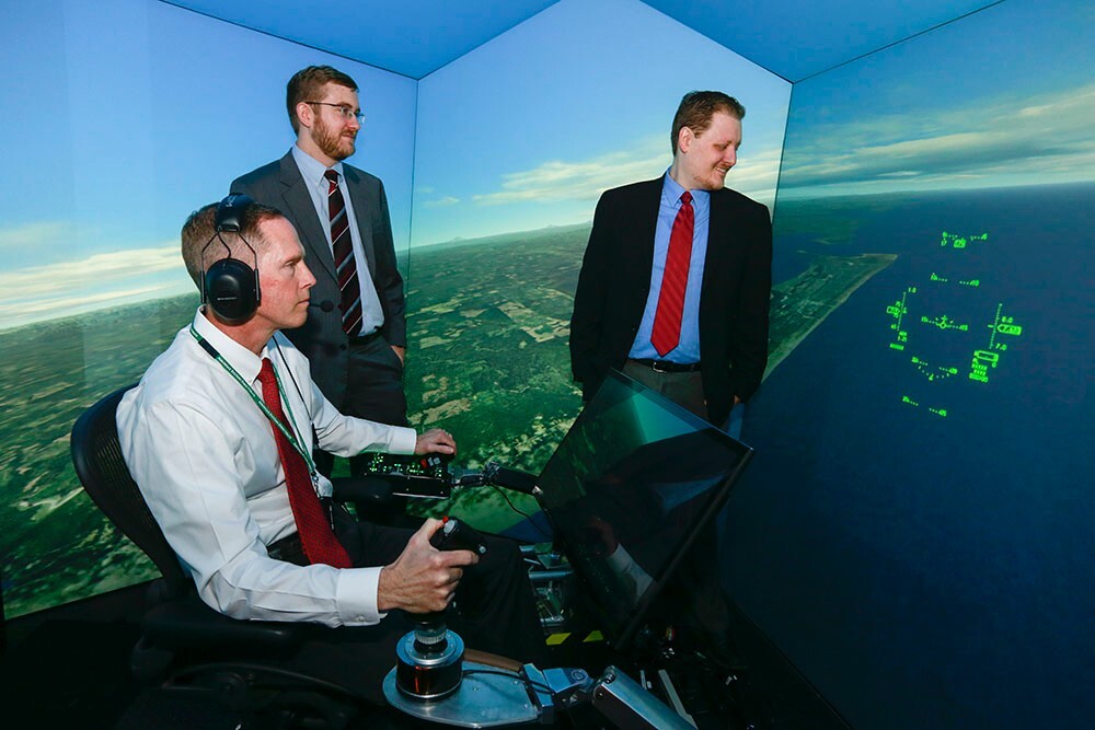Standing at left is Psibernetix President and CEO Nick Ernest. David Carroll, also of Psibernetix, is standing at right. Seated at the simulator controls is retired U.S. Air Force Colonel Gene Lee