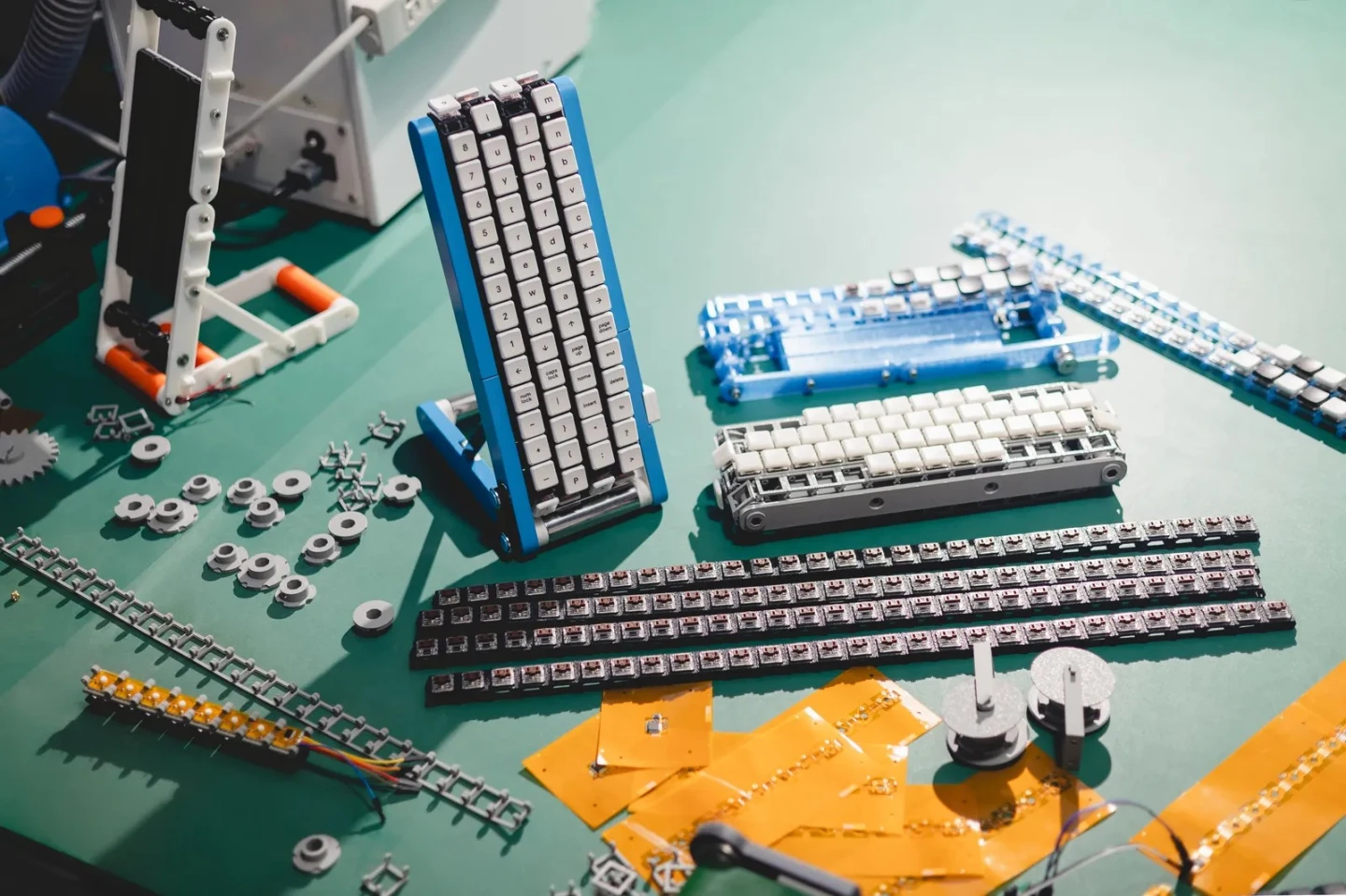 3D-printed chassis components, belt tracks, and circuit boards sit on a workshop bench, reflecting the open-source DIY nature of the project