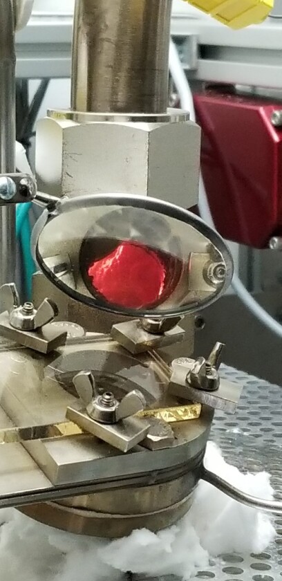 The red material is radioactive tank waste from an underground storage tank at Hanford being illuminated by the molten glass below as it is vitrified into a solid glass for the first time in continuous process
