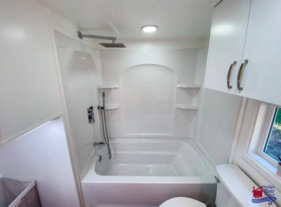 The Sandy tiny house's bathroom includes a bath and shower, plus a vanity sink, and a flushing toilet