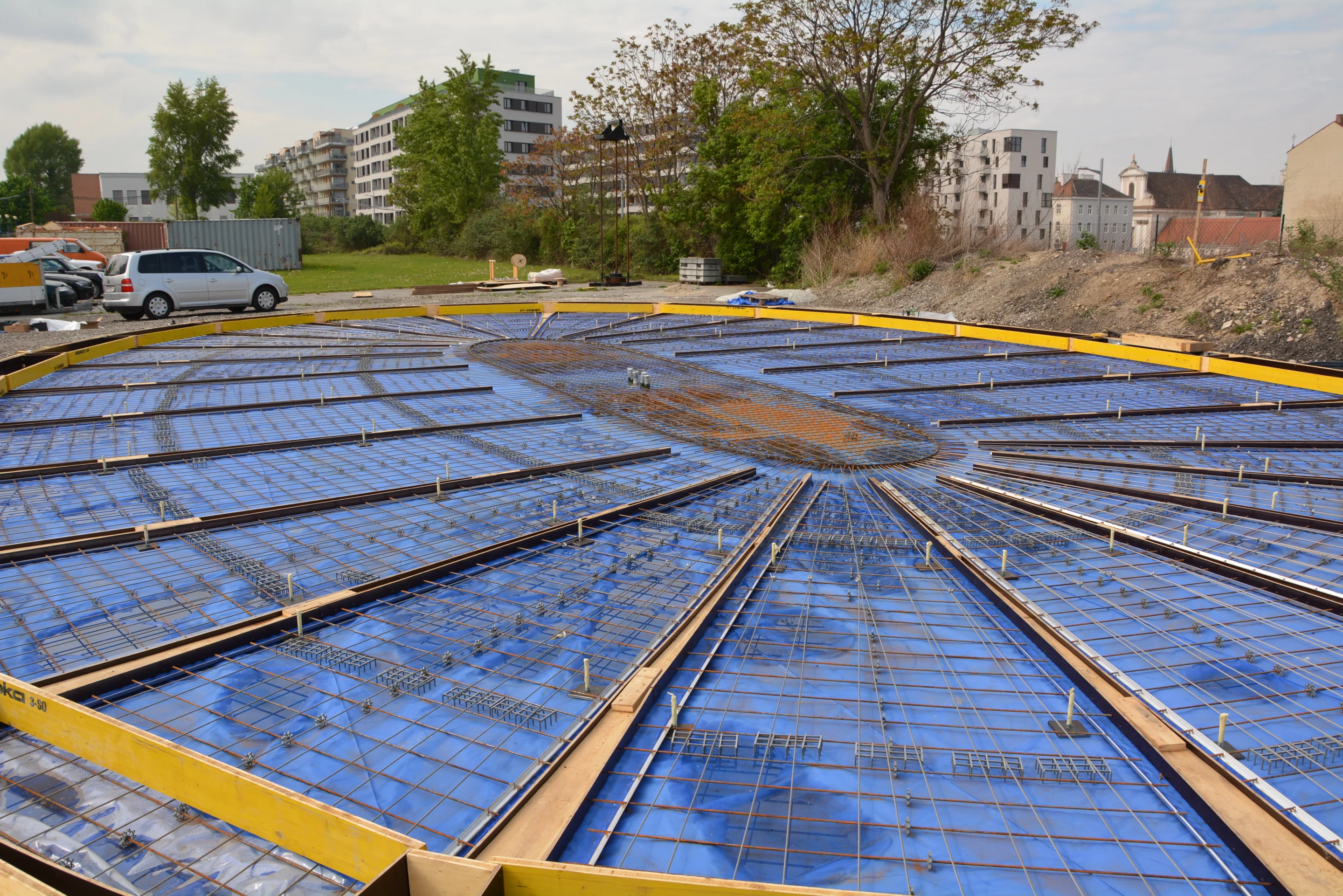 First, a number of flat rebar forms are laid out side-by-side on the ground at the building site, on top of a deflated plastic air cushion