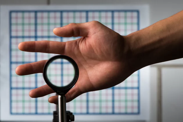 The multidirectional "perfect paraxial" cloak bends light around the hand to show the grid on the wall two meters away with correct color, spacing and magnification (Photo: J. Adam Fenster/University of Rochester)