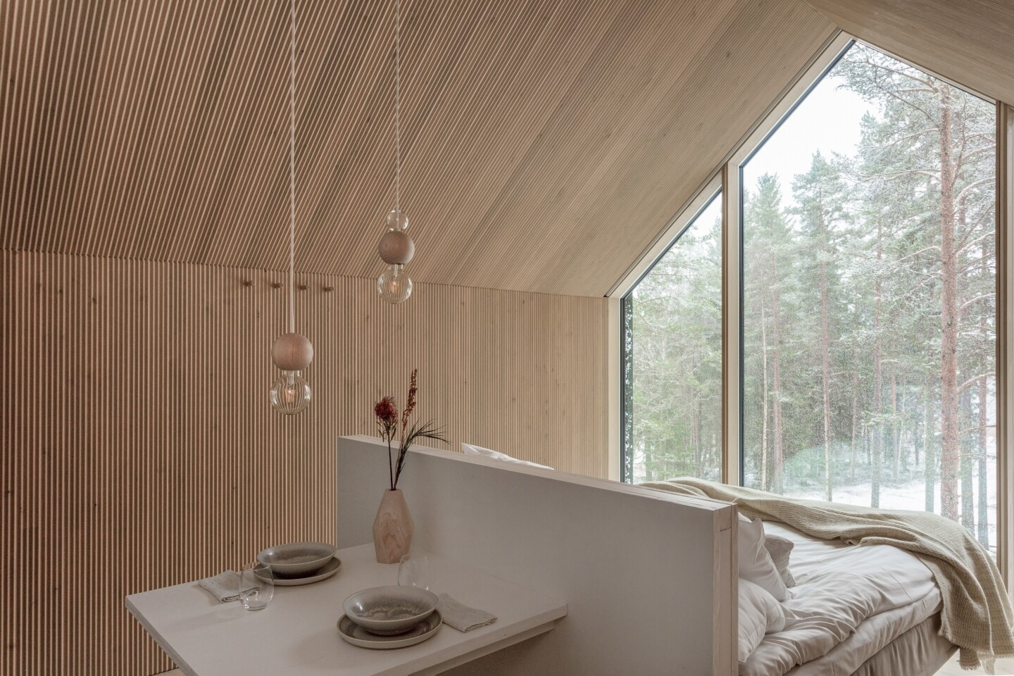 The bedroom is strategically positioned in front of the glass feature wall, allowing guests to enjoy the forest scenery while remaining warm and cozy in bed
