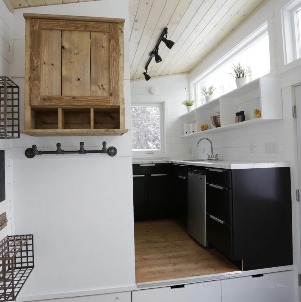 The Open Concept Rustic Modern Tiny House's raised kitchen area has storage space beneath