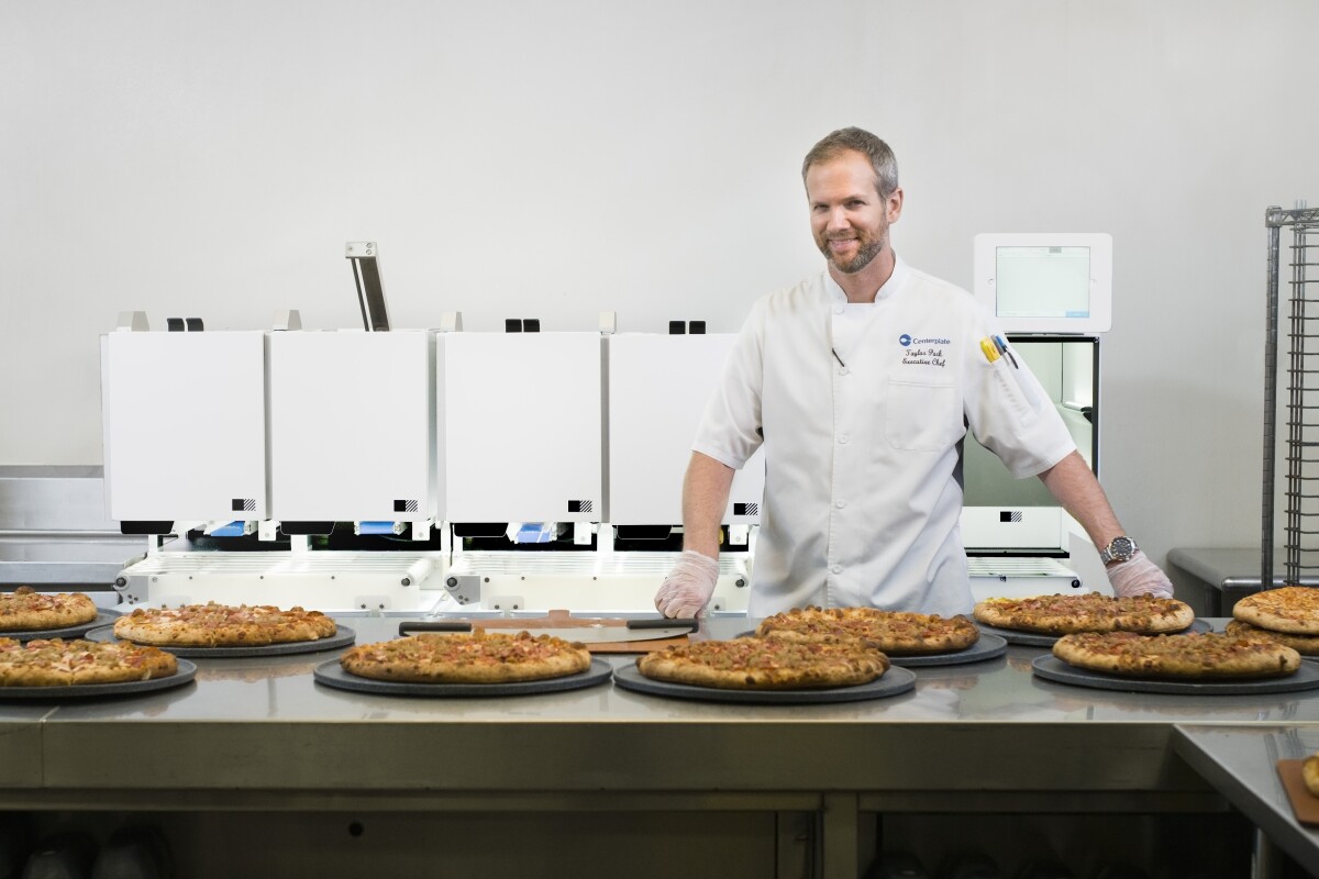 Centerplate Executive Chef Taylor Park stands in front of Picnic's automated pizza assembly robot at T-Mobile Park