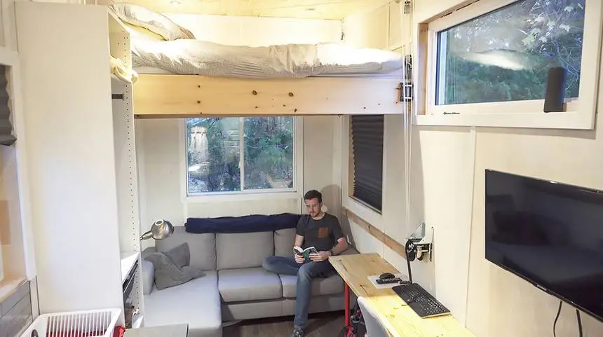 The tiny home consists of a cozy living area positioned underneath the queen bed