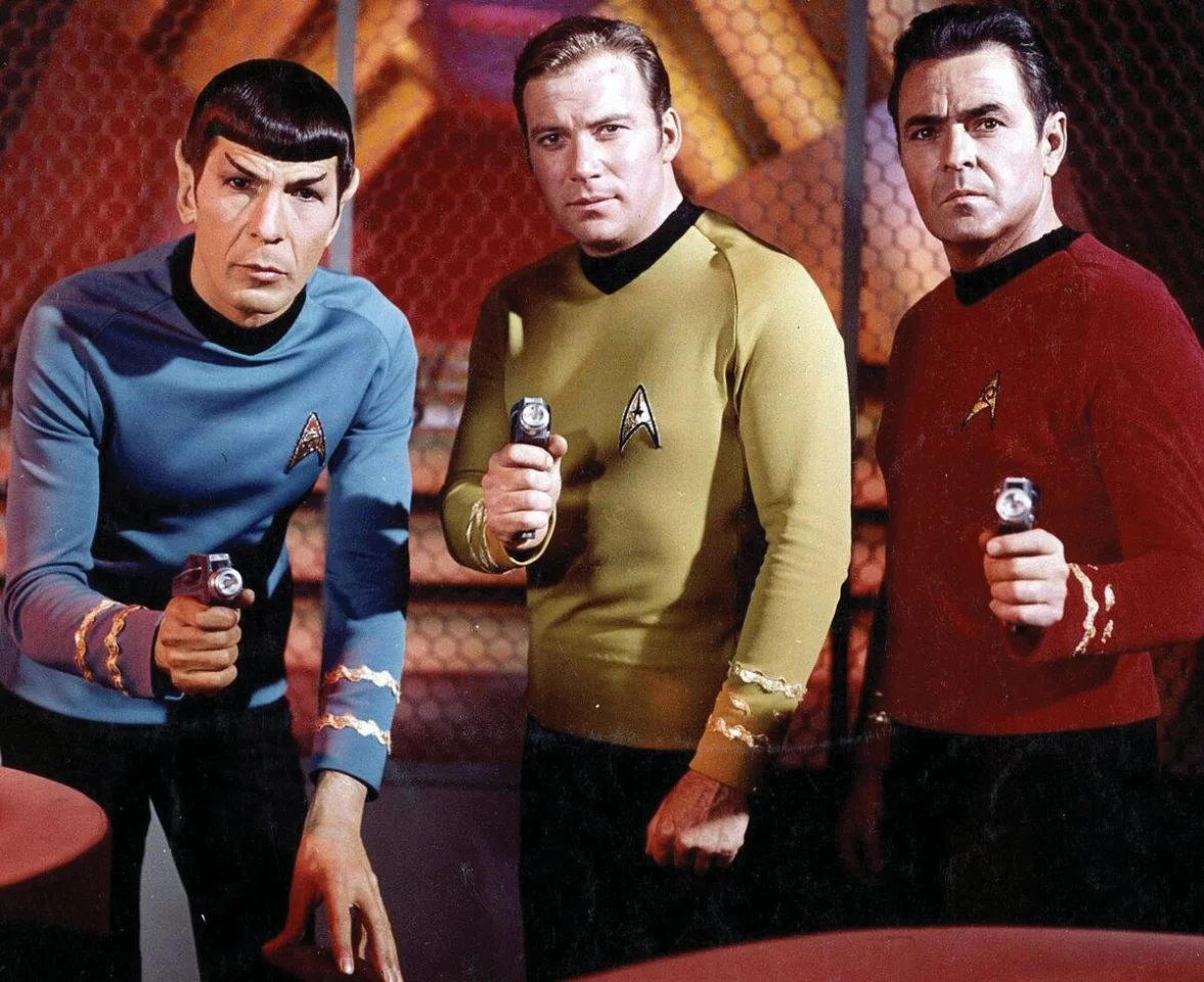The original series of Star Trek was set in the Milky Way galaxy during the 2260s. The ship and crew are led by Captain James T. Kirk (William Shatner - center), First Officer and Science Officer Spock (Leonard Nimoy - left), and Chief Medical Officer Leonard H. "Bones" McCoy (DeForest Kelley -right), all holding Type-2 Phasers.