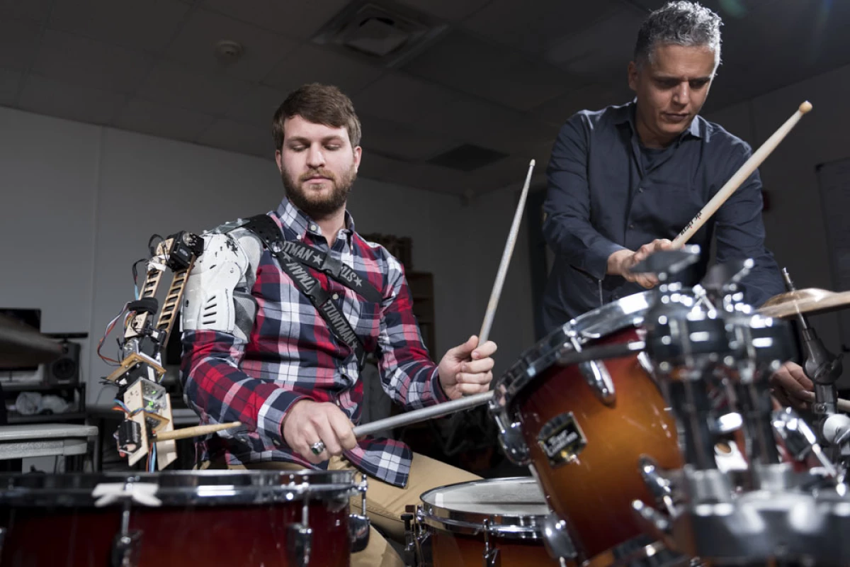 Tyler White (left) with the "third arm" robotic drumming arm accompanied by Professor Gil Weinberg (right)