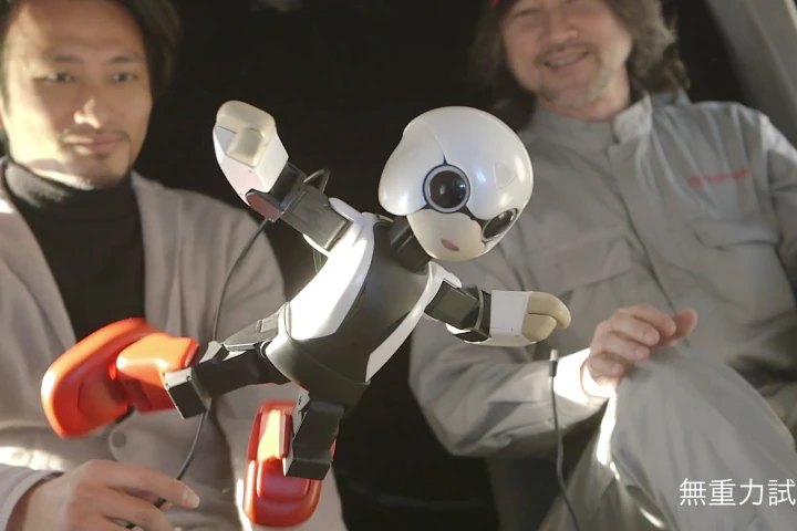 Kibo the Japanese communication robot floats in zero gravity aboard an airplane with its creator, Tomotaka Takahashi (left background)