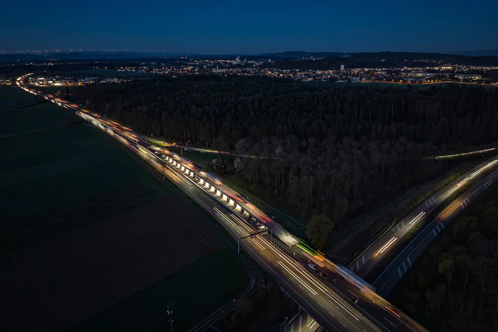 The ASTRA Bridge allows highway traffic (streaks of light in photo) to pass overtop of a sheltered roadwork space (lit-up area with supports)