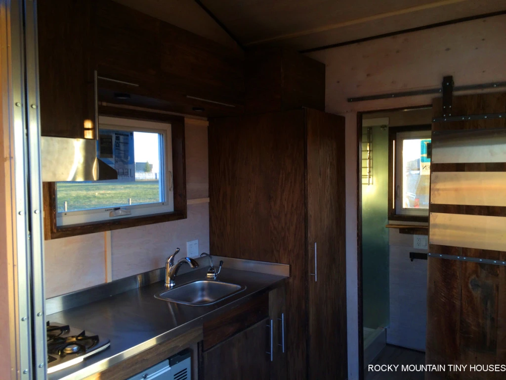The kitchenette features a chest refrigerator, side pantry, a two-burner cooktop, and a folding dining table
