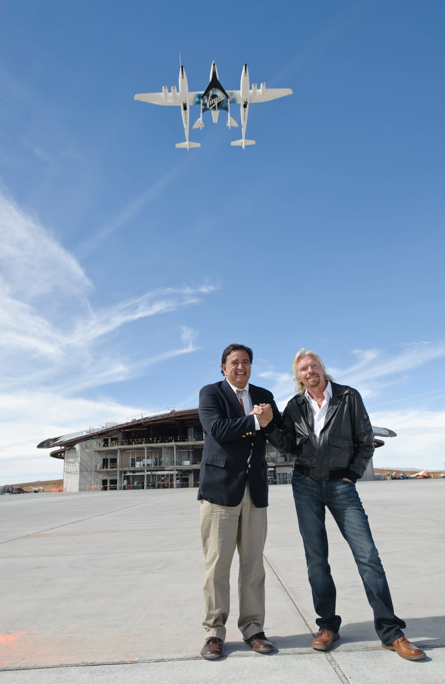 Sir Richard Branson and Governor Richardson in front of Spaceport America with VMS Eve and VSS Enterprise above (Photo: Jeffrey Vock)
