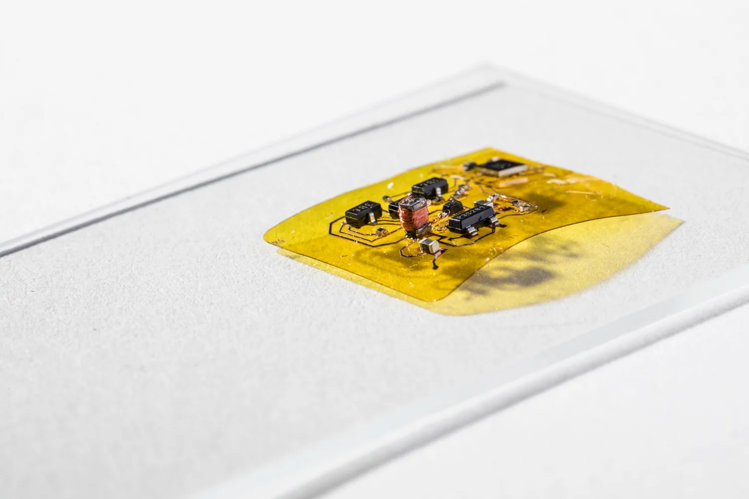 The engineers designed a flexible circuit (yellow) with a boost converter (copper coil and black boxes at left) that boosts the seven volts coming from the photovoltaic cell into the 240 volts needed for flight – this circuit also has a microcontroller brain (black square box in the top right) that lets RoboFly control its wings