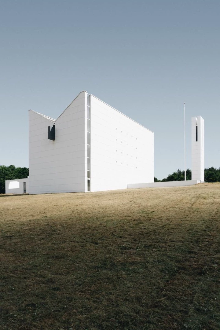 Enghøj Church in Denmark is defined by its geometric design, stark white facade, and sloping roof