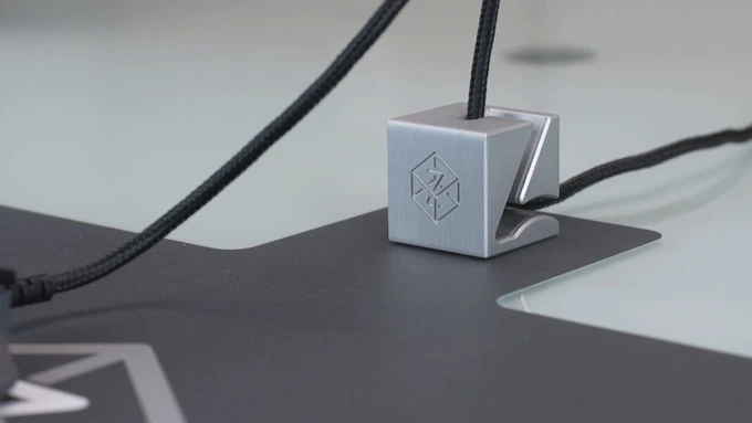 An aluminum cube attached to the mouse mat holds the cable off the desk, reducing drag