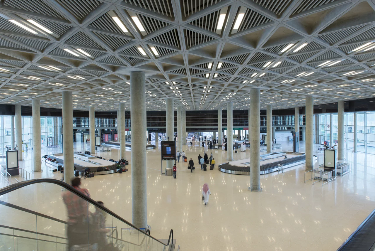 Departure gates are arranged in a line on opposite sides of a central building, with check-in areas, shops, restaurants, lounges, and other passenger services in the middle