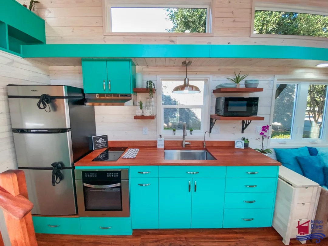 The Sandy tiny house's kitchen includes an oven, electric cooktop, fridge/freezer, microwave, and lots of cabinetry