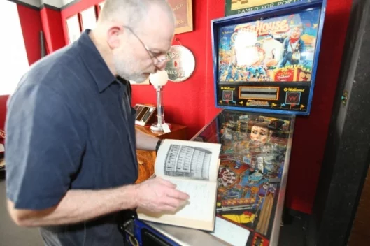 Bennett-Levy leafing through the world's first computer manual atop a pinball machine
