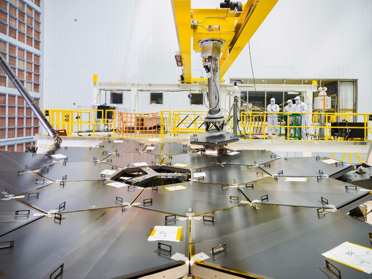 A team of NASA engineers use a robot arm to install the final mirror to the structure of the JWST