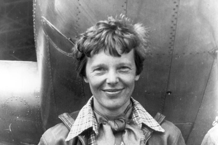 Amelia Earhart, standing under the nose of her Lockheed Model 10 Electra aircraft