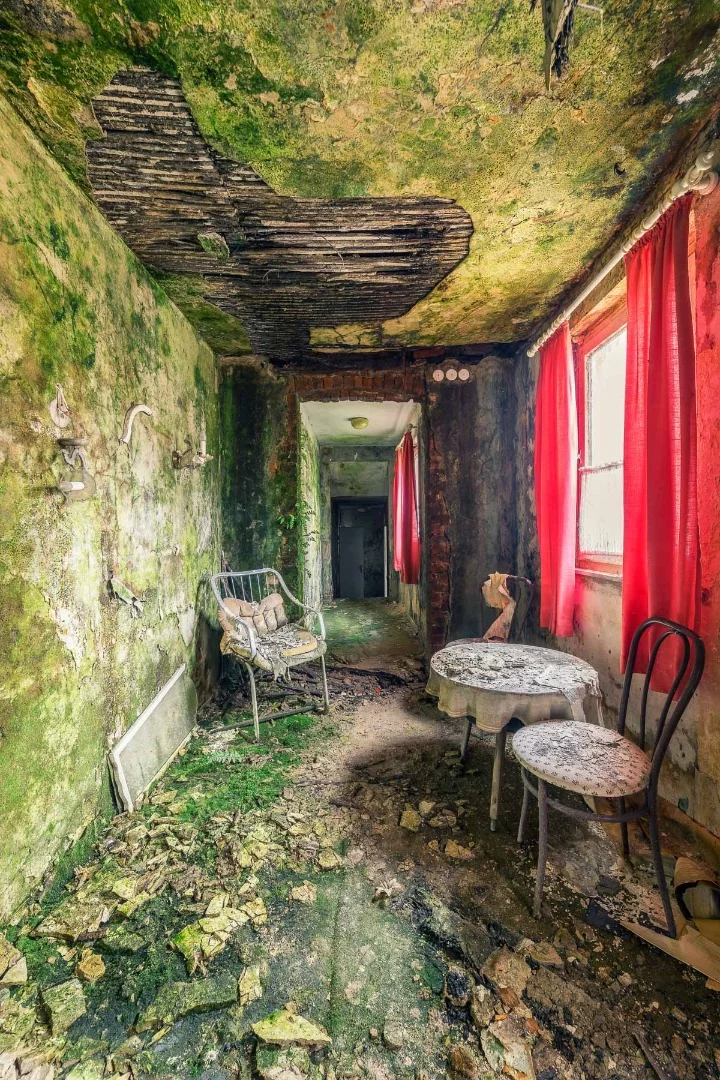 Only the red curtains stand apart from the encroaching green of nature in this decomposing hotel