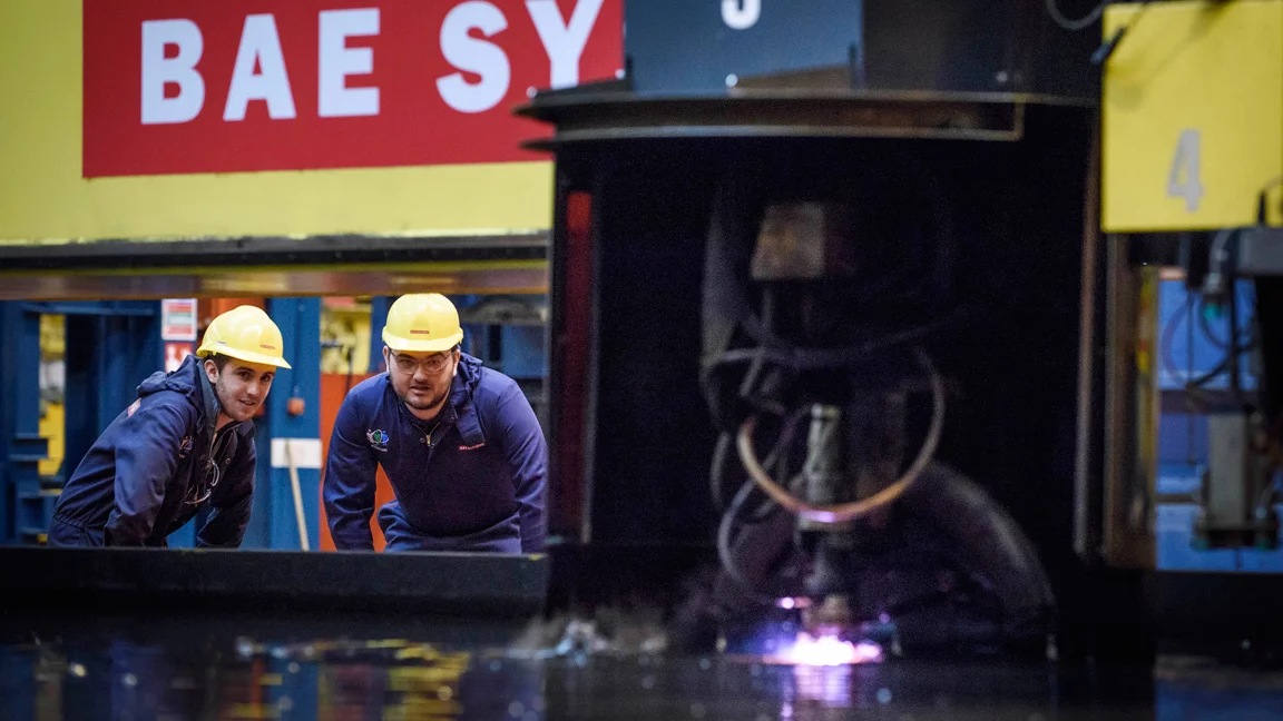 Workmen watch the first steel being cut