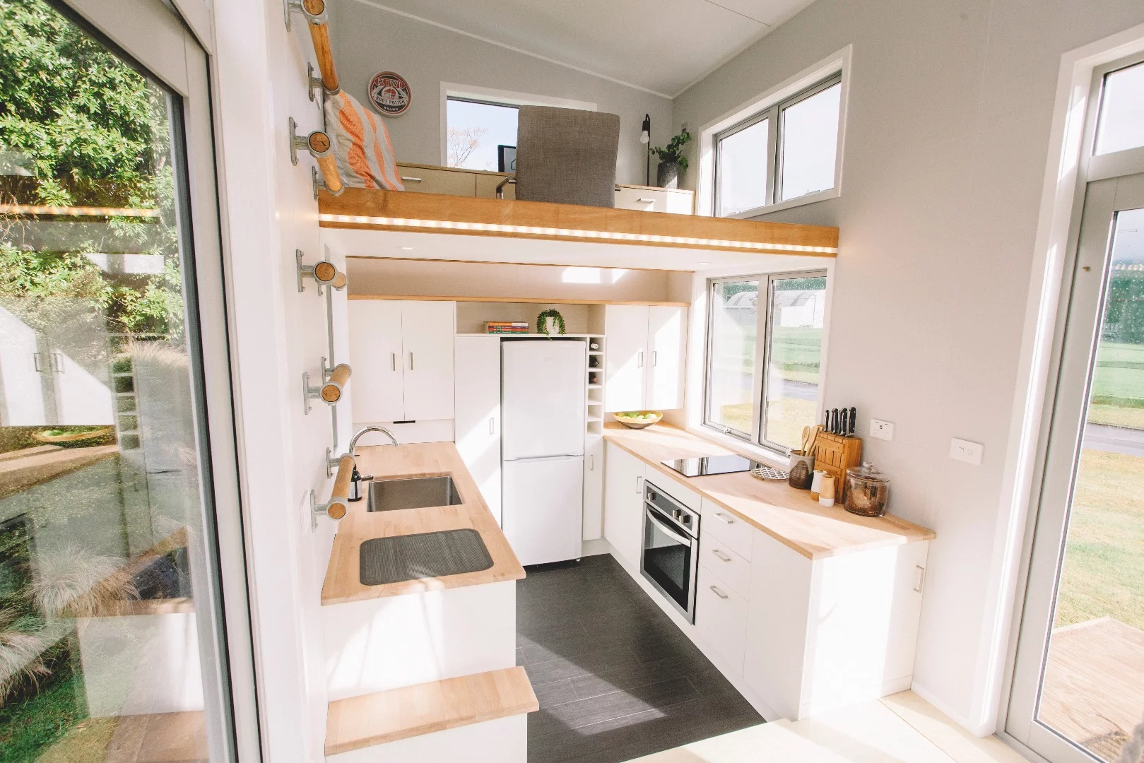 The Millennial Tiny House's kitchen includes full-size fridge, two-burner stove, and sink