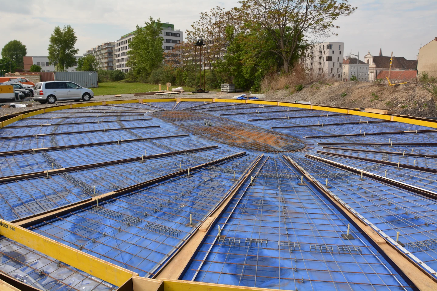 First, a number of flat rebar forms are laid out side-by-side on the ground at the building site, on top of a deflated plastic air cushion