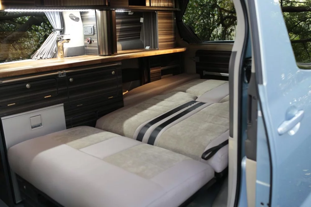 The older EcoCamper uses the same Toyota Alphard Hybrid base but features a full kitchen block and narrower bed/two-seat bench