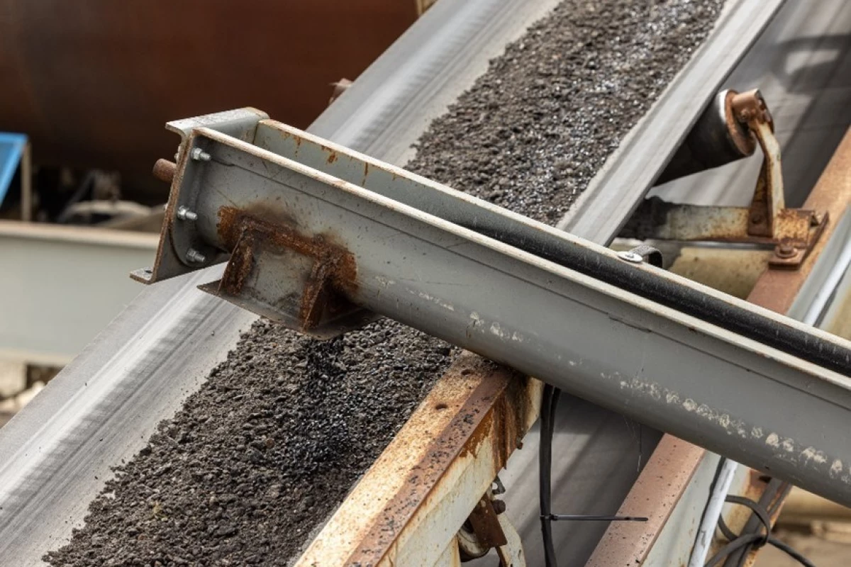 An auger (foreground) adds Recycled Toner Pellets to an asphalt mix on a feeder belt