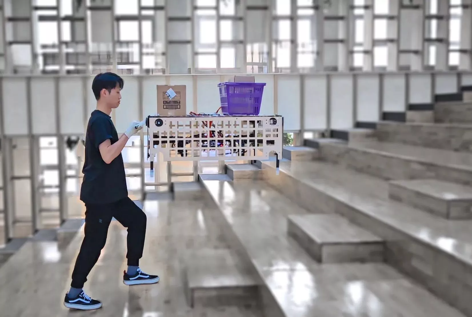 The Palletrone flies at roughly chest height and keeps the upper cargo platform level while a human operator pushes it around