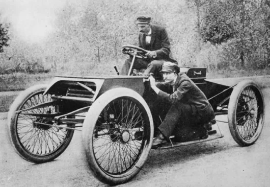 Henry Ford at the wheel of Sweepstakes with Spider Huff posed in his position as riding mechanic.